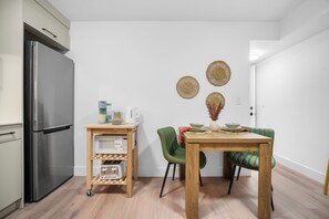 A kitchen with a stainless steel refrigerator, a wooden table with chairs, and a small cart with kitchen appliances.
