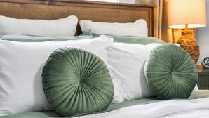 Un lit bien fait, avec des oreillers verts et blancs, une tête de lit en bois et une lampe de chevet.
