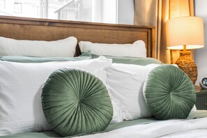 A neatly made bed with green and white pillows, a wooden headboard, and a bedside lamp.