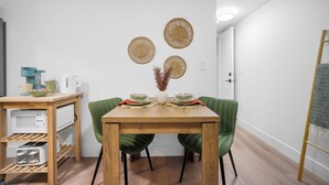 Un coin repas comprenant une table en bois, deux chaises vertes, un vase blanc contenant des plantes séchées et trois éléments de décoration murale en fibres tressées.