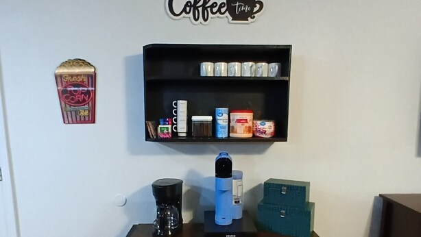 A coffee-themed decor with a coffee machine, a shelf with coffee-related items, and a wall sign.