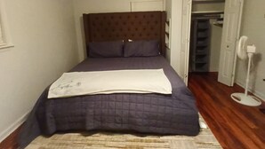 A bedroom with a bed, a headboard, a bedside table, a nightstand, a closet, and a fan.