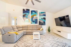 Ein modernes Wohnzimmer mit einem grauen Ecksofa, einem weißen Couchtisch, abstrakter Wandkunst, einem Flachbildfernseher und einem gemusterten Teppich.
