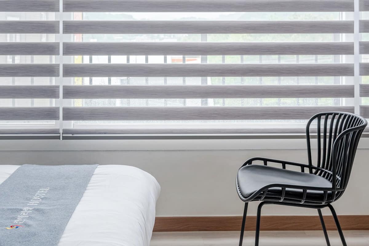 Una habitación de hotel con una cama, una silla y persianas horizontales.