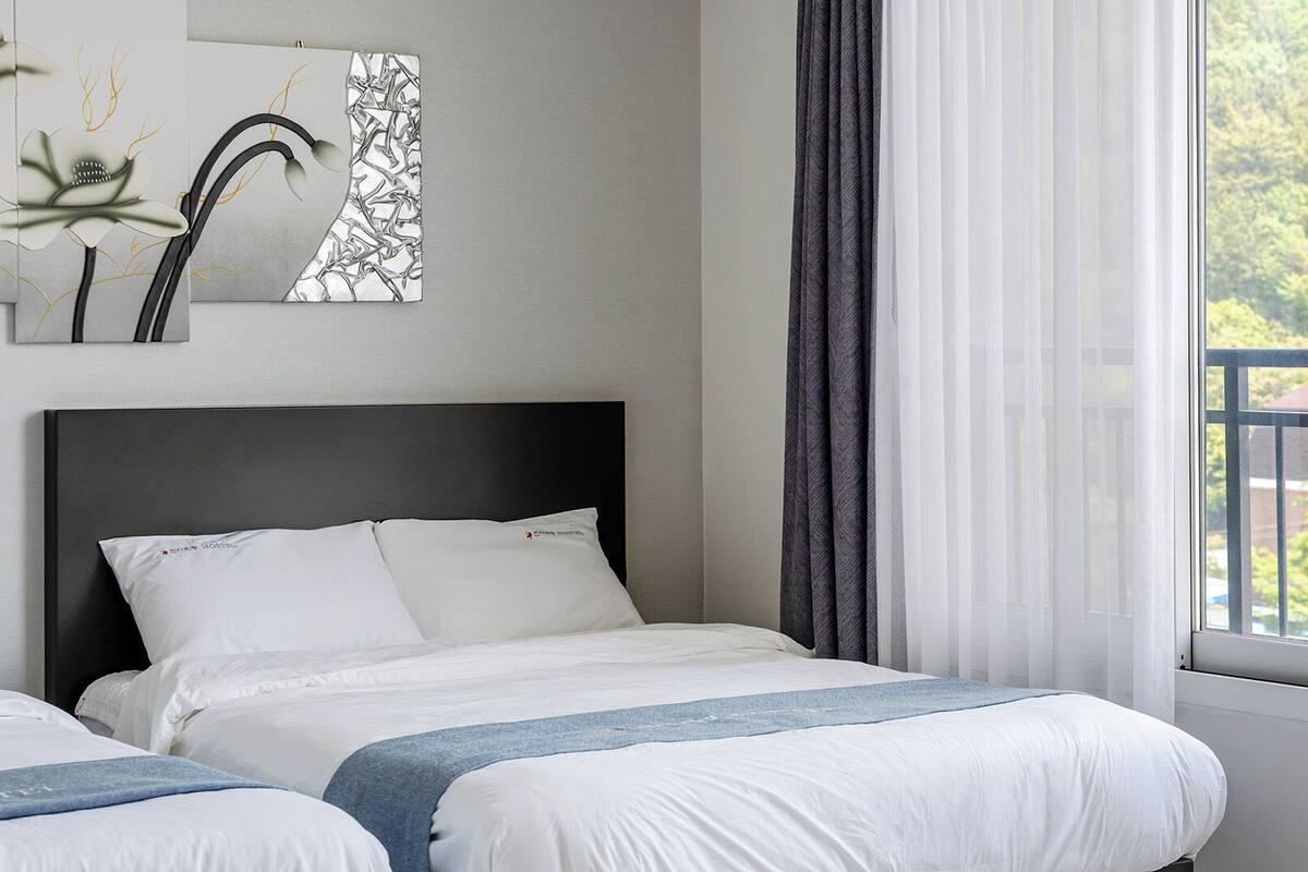 Una habitación de hotel con una cama, una ventana con cortinas y vistas a la vegetación, además de una obra de arte colgada en la pared.
