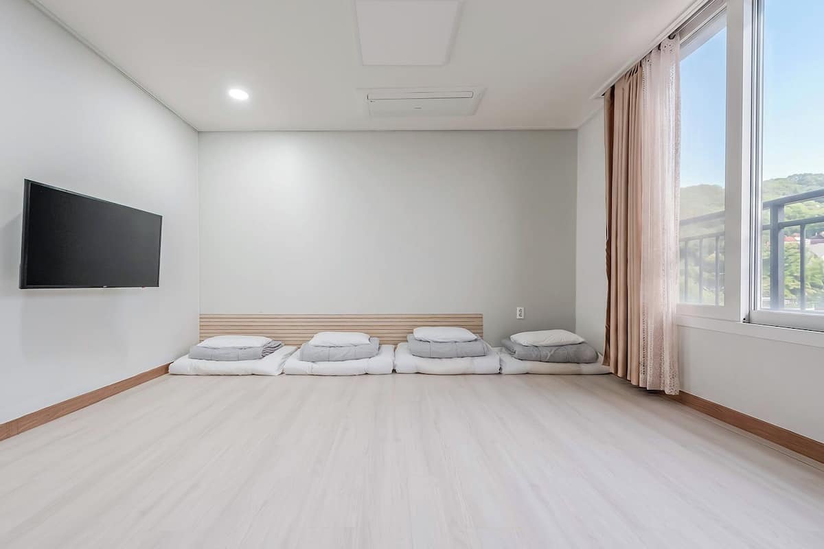 Habitación de hotel con televisor de pantalla plana, cama con almohadas, ventana con cortinas y suelo de madera claro.