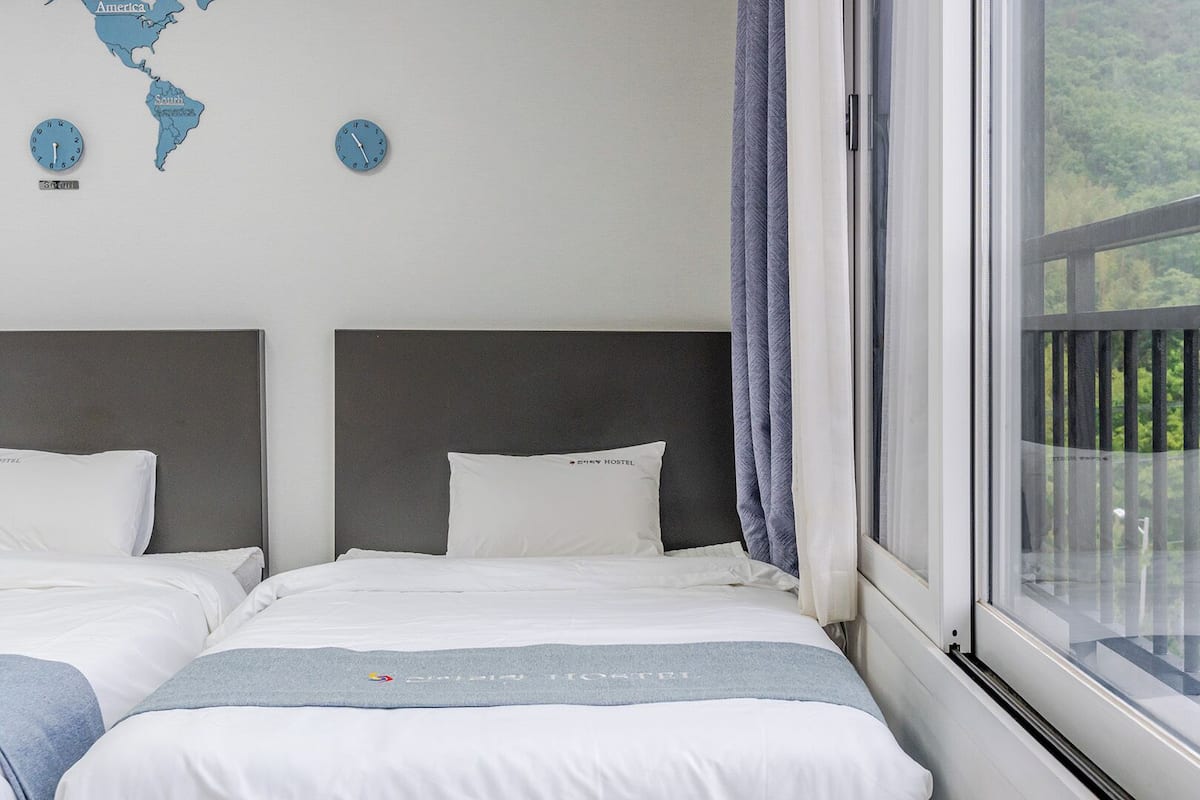 Habitación de hotel con dos camas, un mapa del mundo en la pared y ventana con vistas a zonas verdes.