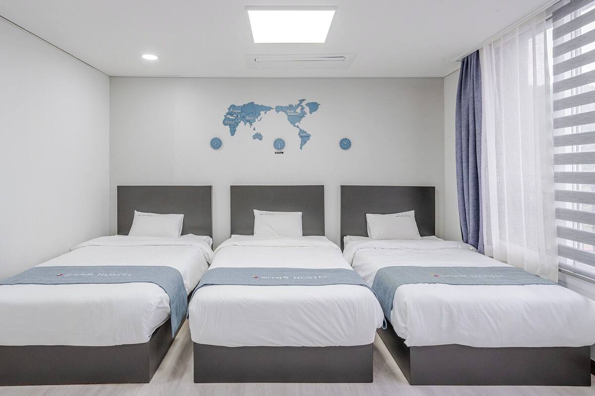 Una habitación de hotel con tres camas, un mapa del mundo en la pared y una ventana con cortinas.