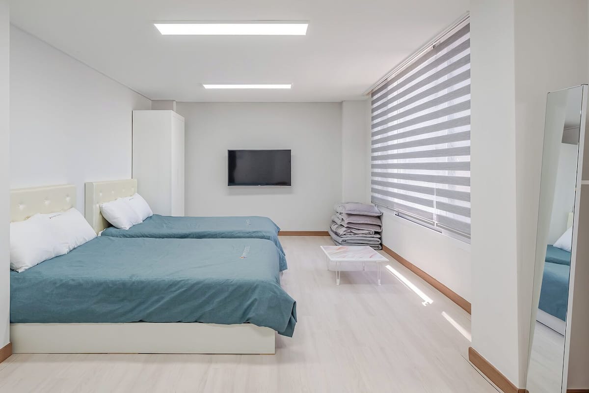 Un dormitorio con dos camas, televisión, armario y ventana con persianas.