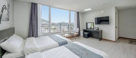 Quarto de hotel com duas camas, uma escrivaninha, uma cadeira, televisão e uma janela grande com vista.