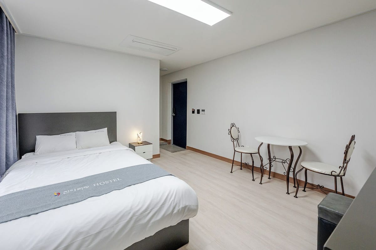 Una habitación de hotel con cama, mesita de noche, lámpara y una pequeña mesa con sillas.
