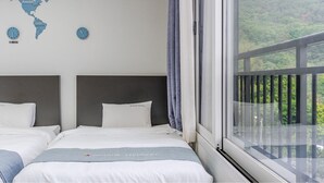 Ein Hotelzimmer mit zwei Betten, einer Weltkarte an der Wand und einem Fenster mit Blick auf Grünflächen.