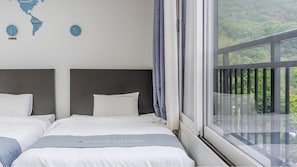 Ein Hotelzimmer mit zwei Betten, einer Weltkarte an der Wand und einem Fenster mit Blick auf Grünflächen.