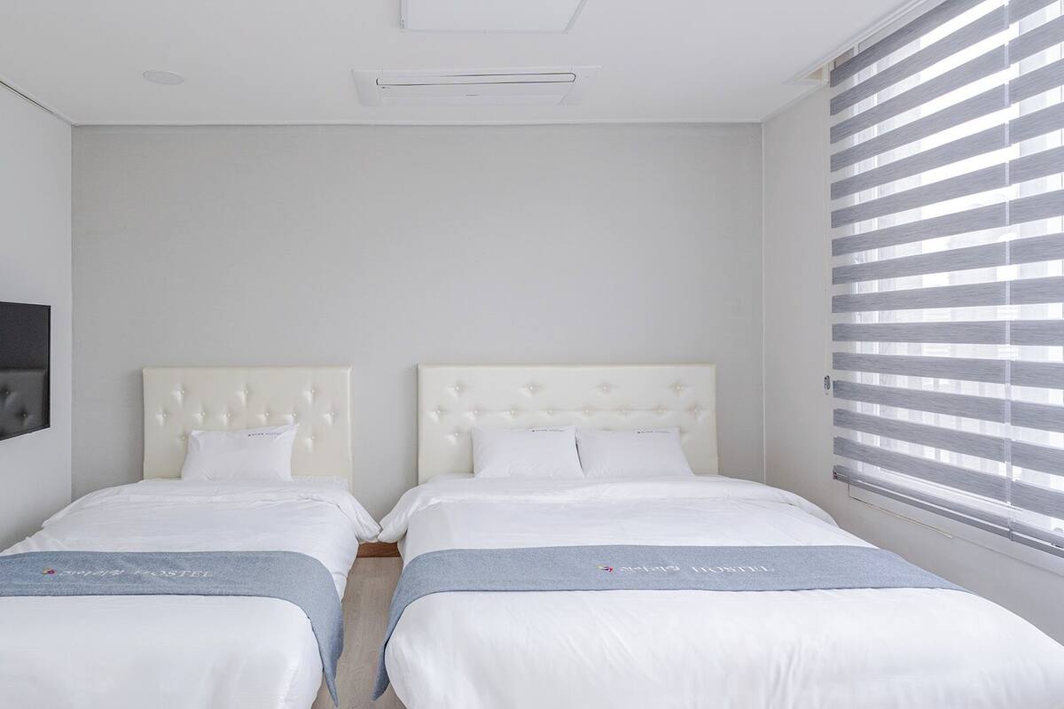 Una habitación de hotel con dos camas, un televisor de pantalla plana y una ventana con persianas.