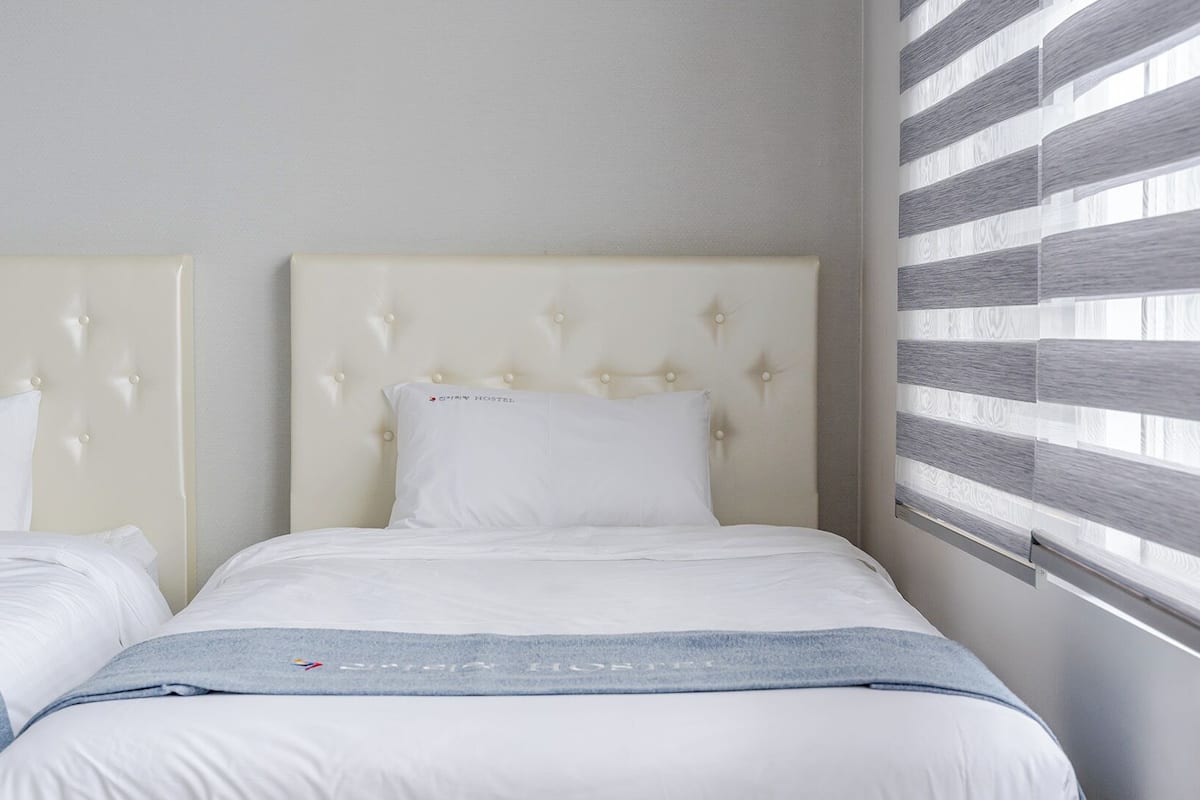 Habitación de hotel con cama, cabecera y ventana con persianas.