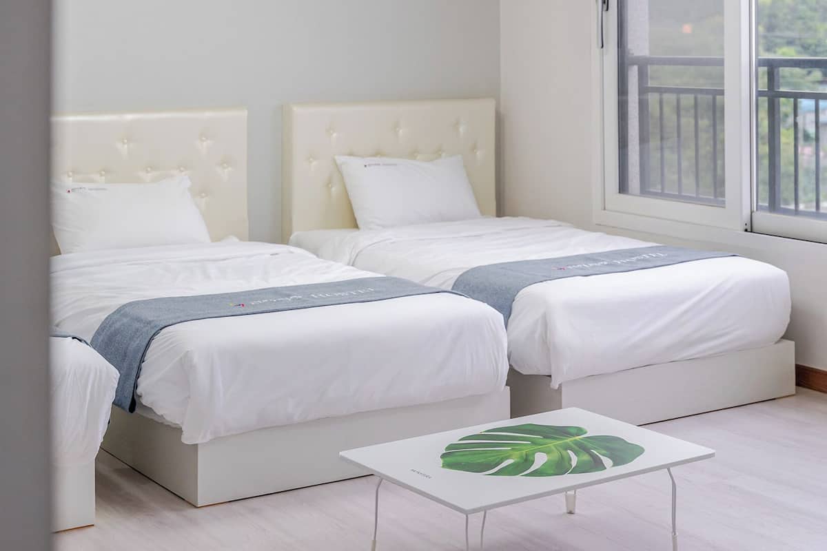 Un dormitorio con dos camas, una mesita y una ventana con vistas al exterior.