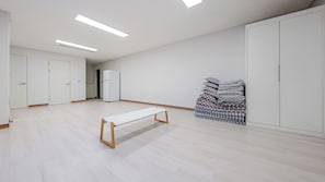 A spacious room with a long bench, a refrigerator, and neatly stacked bedding. - Yeosu Jin Arirang Hostel Pension (Yeosu)