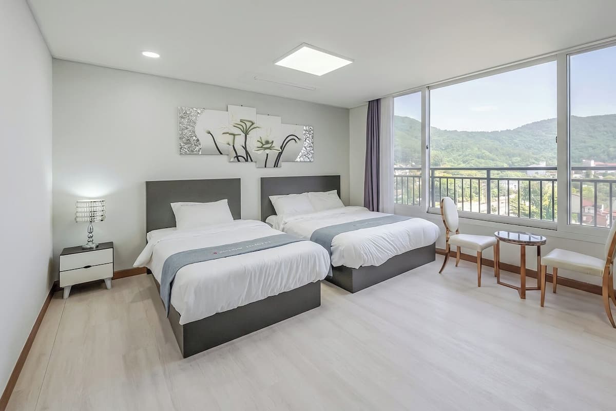 Una habitación de hotel moderna con dos camas, una mesita, una silla y un balcón con vistas.