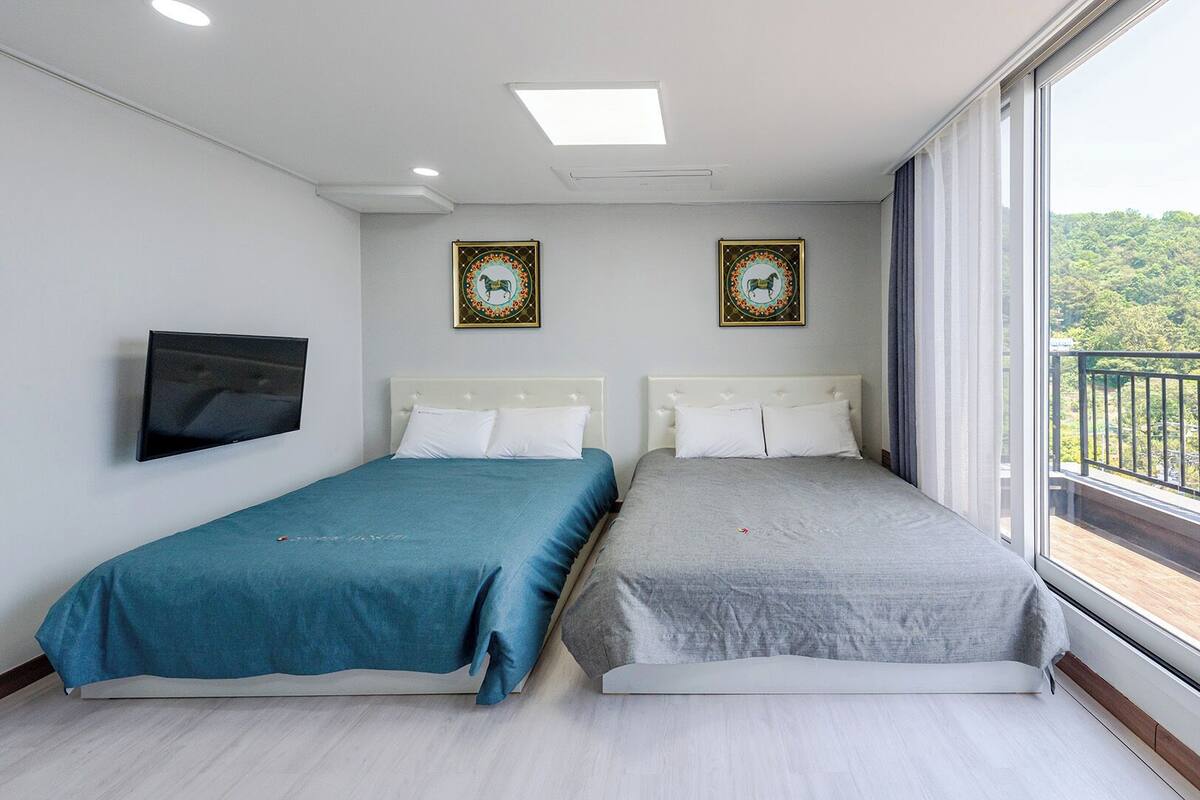 Habitación de hotel con dos camas, televisión y balcón con vista a zonas verdes.