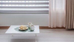 Ein kleiner Tisch mit einer Platte Gebäck und zwei Kaffeetassen, ein Fenster mit Jalousien und einem Vorhang.