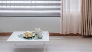 Ein kleiner Tisch mit einer Platte Gebäck und zwei Kaffeetassen, ein Fenster mit Jalousien und einem Vorhang.