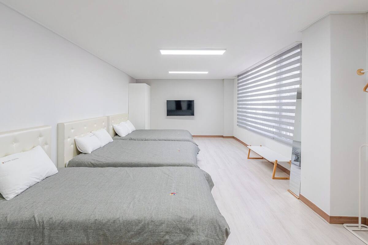 Habitación de hotel con dos camas, un televisor en la pared y una ventana con persianas.
