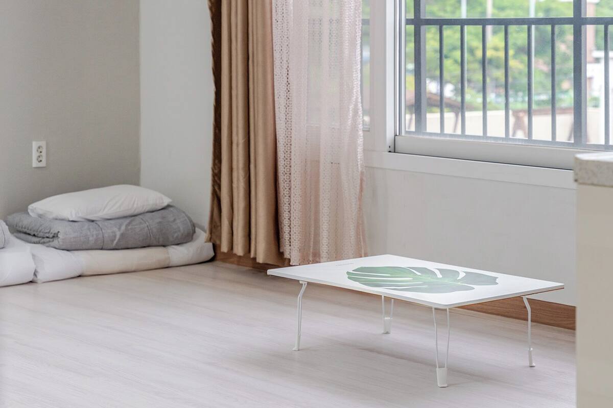 Una habitación con una cama, una mesita, un ventanal y una cortina.