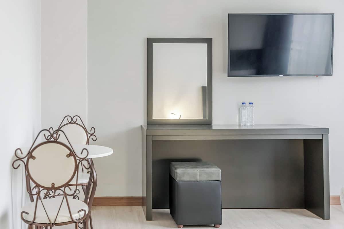Una habitación moderna con un escritorio gris, un pequeño taburete gris, una silla metálica redonda y un televisor de pantalla plana montado en la pared.