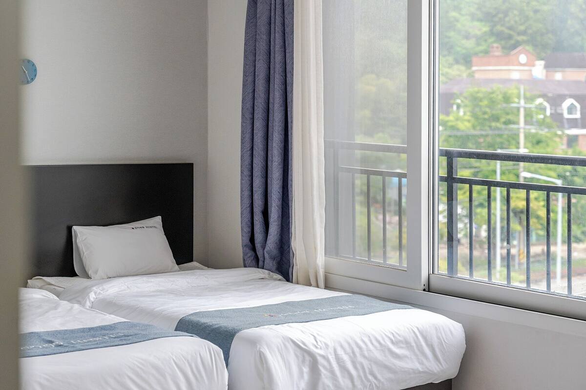 Una habitación de hotel con dos camas, una ventana con vistas a edificios y un cabecero.