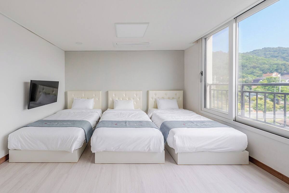 Un dormitorio con tres camas, un televisor y un ventanal con vista a una colina.