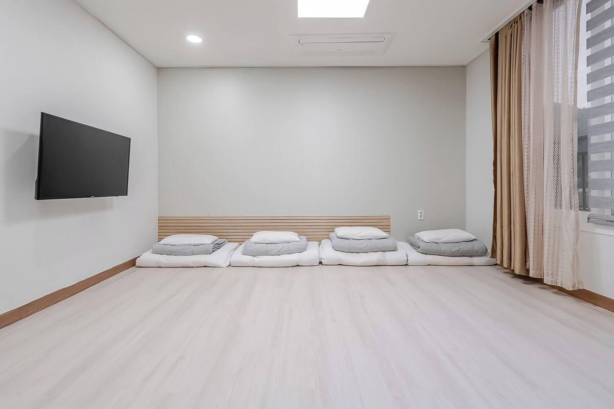 Una habitación con televisión de pantalla plana montada en la pared, una cama con cabecera de madera y una ventana con cortinas.
