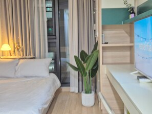 Habitación de hotel con cama, planta en maceta, televisor y ventana con cortinas.