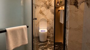 Une salle de bain moderne avec un mur en marbre, des toilettes séparées par une paroi de verre et un porte-serviettes.