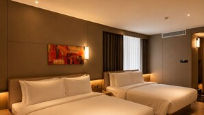Une chambre d’hôtel avec deux lits, un tableau au mur et une fenêtre avec des rideaux.