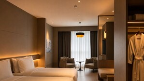 Une chambre d’hôtel avec deux lits, un coin salon, une télévision et un peignoir accroché au mur.