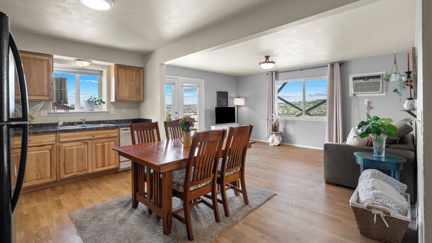 Una cocina amplia con armarios de madera, una mesa de comedor y sillas. Hay un televisor, una ventana con vistas y una planta en el alféizar.