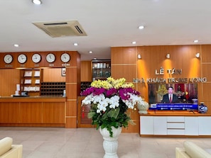 Ein Empfangsbereich mit einem Holzbüro, einer großen Blumenkomposition, Uhren an der Wand und einem Fernsehbildschirm, der eine Nachrichtensendung zeigt.