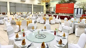 A banquet hall with round tables, white chairs, and a large red banner. - Nha Khach TW (Hanoi)