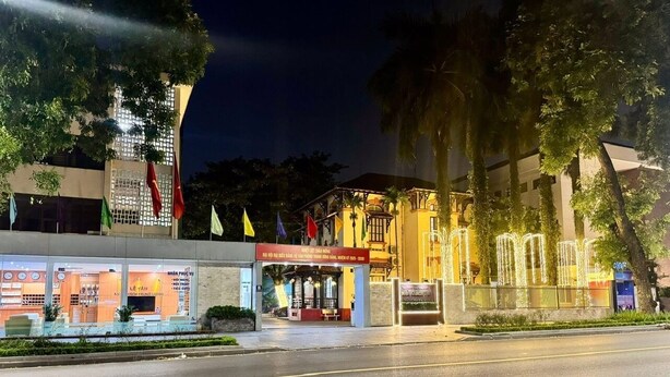 A hotel entrance with a covered area, flags, and a building with a balcony. - Nha Khach TW (Hanoi)