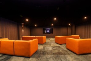 A cinema room with orange seating, a screen, and ceiling lights.