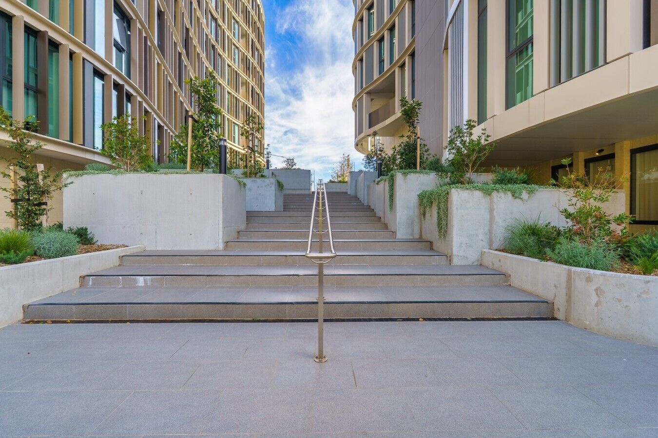 A modern building with a central staircase leading to a higher floor, surrounded by greenery and concrete walls.