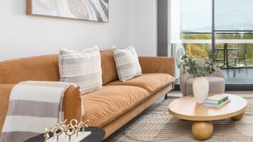 Un salon moderne avec un canapé, des coussins, une table basse et une vue sur l’extérieur.