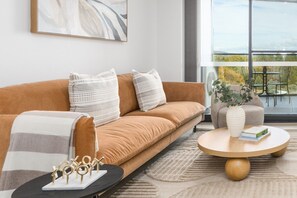 A modern living room with a sofa, pillows, a coffee table, and a view of the outdoors.