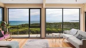 Ein geräumiges Wohnzimmer mit großen Schiebeglasfenstern, einem Sofa, einem Couchtisch und Meerblick.