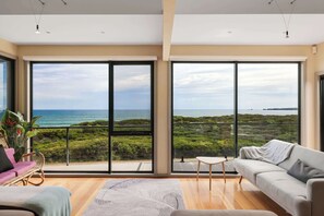 A spacious living room with large sliding glass doors, a sofa, a coffee table, and a view of the ocean. - Amazing Ocean Views with Spa (Surf Beach)