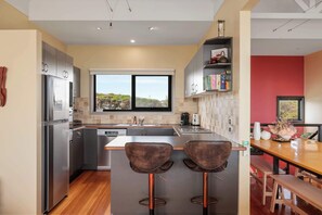 A modern kitchen with a large island, bar stools, and a view of the outdoors. - Amazing Ocean Views with Spa (Surf Beach)