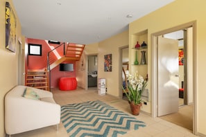 A modern living room with a sofa, a staircase, a flat-screen TV, and a potted plant. - Amazing Ocean Views with Spa (Surf Beach)