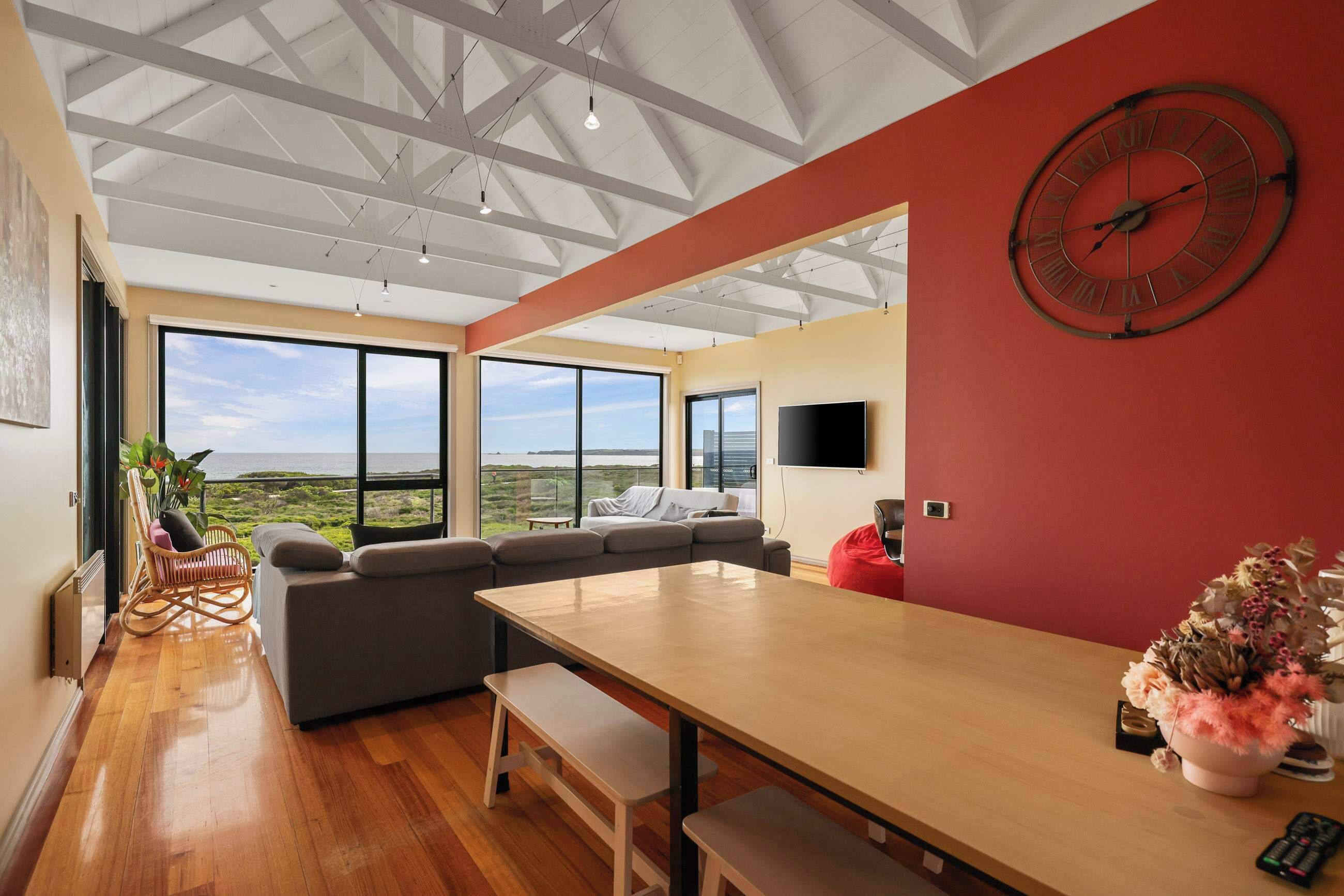 A modern interior with a large dining table, a sofa, and a red accent wall.