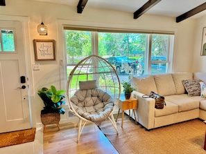 A cozy living room with a cushioned chair, a sofa, a small side table, and a large window offering a view of the street. - Spacious, beautiful 5 Bed, 2.5 Bath modern house in Saint Paul for extended stay (Saint Paul)