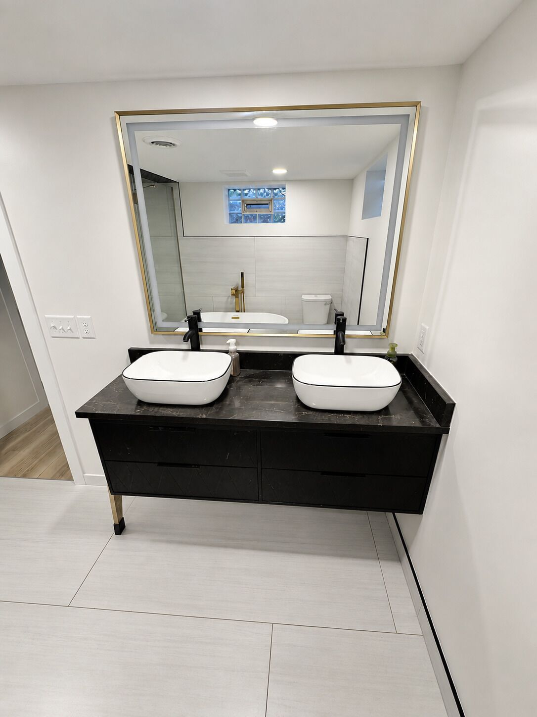 Une salle de bain moderne avec un meuble-lavabo noir, deux vasques blanches et un grand miroir avec un cadre doré.